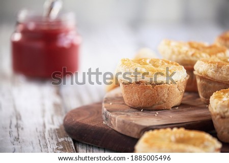 Fresh meat pies on a rustic wood cutting board with ketchup in the background. Selective focus on center pie with extreme blurred foreground and background. Free space for text available.