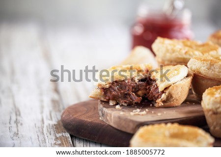 Cut fresh venison meat pies on a rustic wood cutting board with filling visible and ketchup in the background. Selective focus on center pie with extreme blurred foreground and background. Free space 