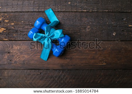 two blue dumbbell with a gift bow and blank paper tag, heart on wooden planks, sport holiday concept