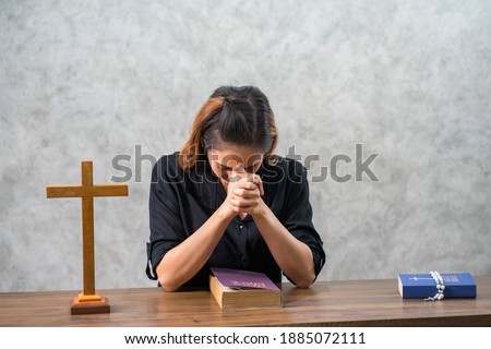 Asian Christian praying with HOLY BIBLE in the church with wooden cross. 