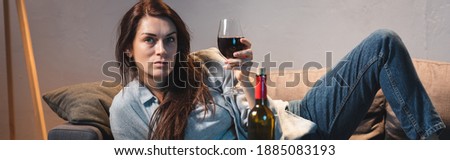drunk, frustrated woman looking at camera while lying with glass of red wine, banner