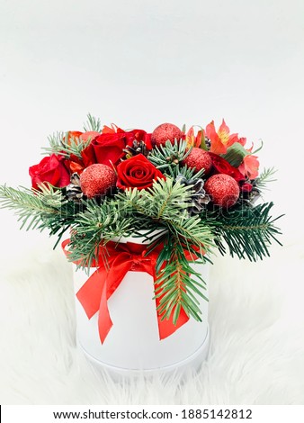 Round box with winter bouquet of fir tree branches, red roses and shining balls with bow in red and green colors