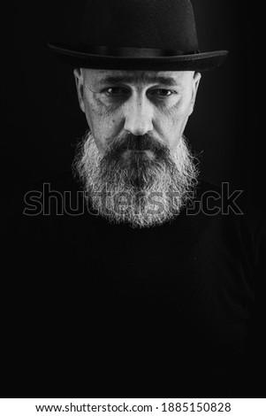 portrait of a young, handsome, emotional, serious man with a gray long beard and a black hat on his head, isolated on a dark background. There is a place for an inscription. black and white photo