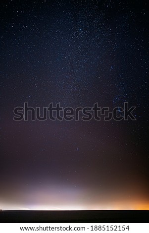 Night Starry Sky With Glowing Stars Above Countryside Landscape. Milky Way Galaxy And Rural Field Meadow In Early Spring. Bright Glowing Stars.