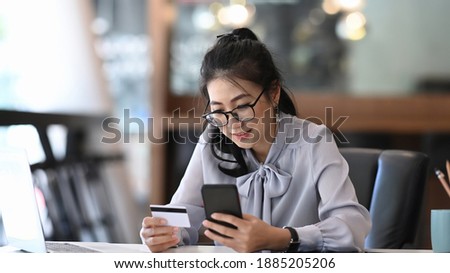 A young woman holding smart phone and credit card making payment online or shopping online.