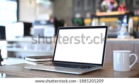 An open laptop computer with blank screen, coffee cup and notebook on wooden desk. Blank screen for graphics display montage.