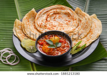 Homemade kerala Porotta or paratha,layered flat bread made using maida or all purpose wheat flour arranged in a black ceramic plate on fresh green banana leafand garnished with onion rings. Royalty-Free Stock Photo #1885213180