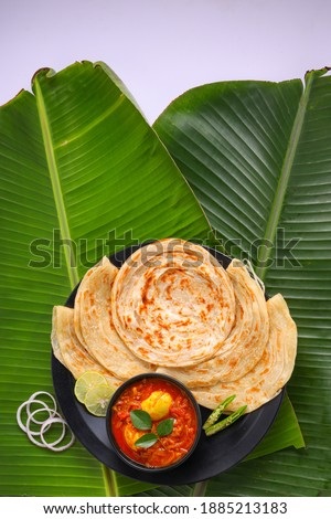 Homemade kerala Porotta or paratha,layered flat bread made using maida or all purpose wheat flour arranged in a black ceramic plate on fresh green banana leafand garnished with onion rings. Royalty-Free Stock Photo #1885213183