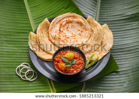 Homemade kerala Porotta or paratha,layered flat bread made using maida or all purpose wheat flour arranged in a black ceramic plate on fresh green banana leaf and garnished with onion rings. Royalty-Free Stock Photo #1885213321