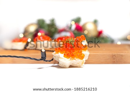 Cropped photo of Bread with red caviar in the form of Christmas trees on a wooden cutting board on the background of a New Year's wreath with a garland
