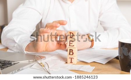 Businessman removes wooden blocks with the word Debt. Reduction or restructuring of tax. Bankruptcy announcement. Refusal to pay loans and invalidate them. Royalty-Free Stock Photo #1885246123