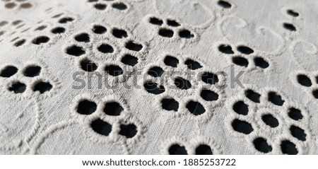 Relief embroidery with a floral print from round holes on white cotton fabric, on a dark background (diagonally,
texture).