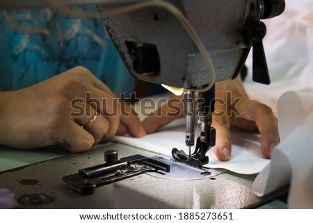 Woman hands with fabric at sewing machine. Seamstress working behind her equipment. Tailoring process, designer workshop, garment industry concept