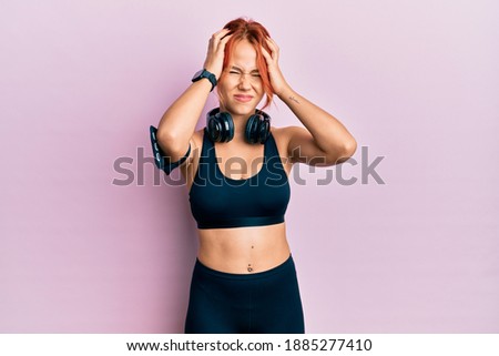 Young beautiful redhead woman wearing gym clothes and using headphones suffering from headache desperate and stressed because pain and migraine. hands on head. 