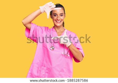 Young hispanic woman wearing doctor uniform and stethoscope smiling making frame with hands and fingers with happy face. creativity and photography concept. 