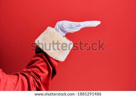 Hand of a man wearing santa claus costume and gloves over red background with flat palm presenting product, offer and giving gesture, blank copy space 