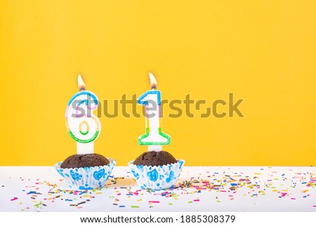 61 number candle on a cup cake with colorful sprinkles and yellow background sixty first birthday anniversary celebrations