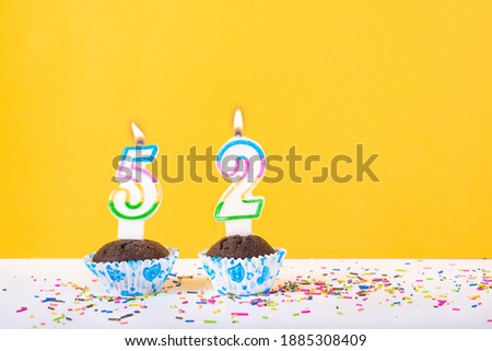 52 number candle on a cup cake with colorful sprinkles and yellow background fifty second birthday anniversary celebrations