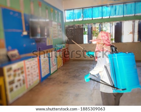 Asian woman with blue tank and spraying classroom rain disinfectant Prevent hand, foot and mouth disease concept.