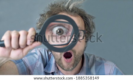 a curious funny surprised Middle-aged  man who is looking at the camera through a magnifying glass. Humorous portrait of a crazy man with no cut hair.