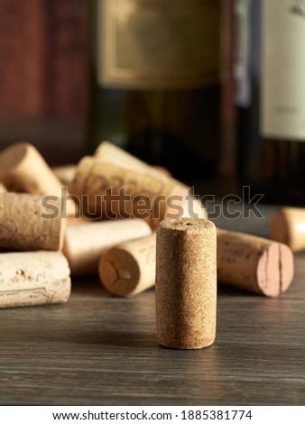 The cork from a bottle of wine stands on a wooden table, against the background of other corks and bottles of wine.