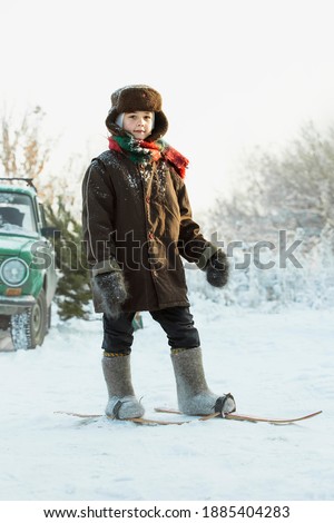 A boy in Soviet clothes is skiing near a green Zhiguli car. Winter vintage picture. Image with selective focus and noise effects and toning