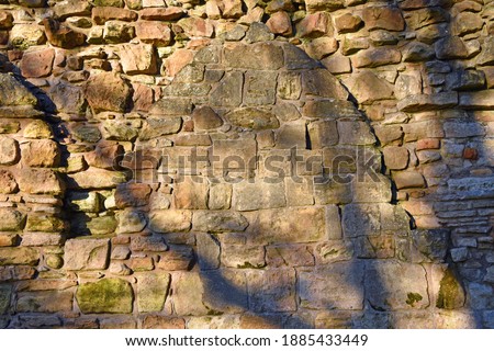 Segment of 11th century stone wall with stone arch and shadows from trees on wall. Ruins of Culross Monastery, Fife, Scotland, UK