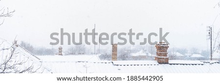Winter rural landscape with snow, roofs and chimneys in snowfall