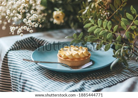 Lemon tart on a blue plate on a striped cloth, decorated with seasonal leaves and flowers