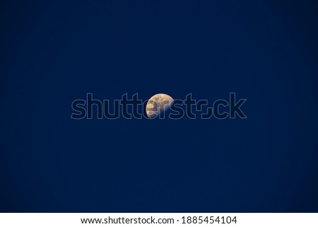 distant crescent moon, with colored surface, isolated on a dark blue twilight sky.