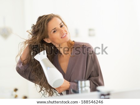 Happy young woman blow drying hair in bathroom Royalty-Free Stock Photo #188546246
