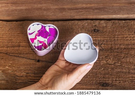 Opening a box in the form of a heart with many bright valentines inside. Box with bright hearts on a wooden surface. Place for inscriptions