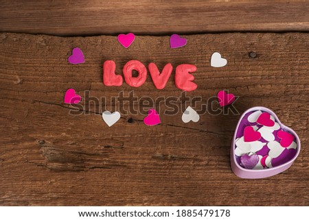 The word "love" is written in bright letters surrounded by small colored hearts of paper. Original confession of love. Romantic postcard with your own hands
