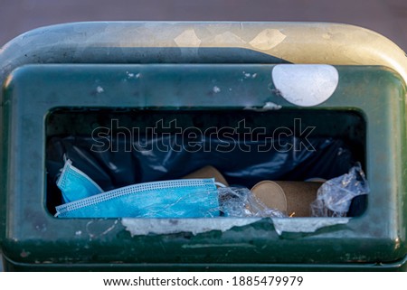 Litter the waste in the bin concept, Selective focus of light blue surgical face masks, Paper coffee cup and plastic thrown away in trash can after use, Waste procedure or medical mask on the street. Royalty-Free Stock Photo #1885479979