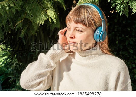 A Pretty Caucasian Young Girl Listening To Music With Blue Headphones In Park