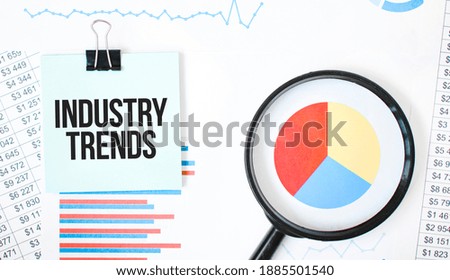 Green card on the white notepad and magnifier on the financial documentation. Text INDUSTRY TRENDS. Business concept
