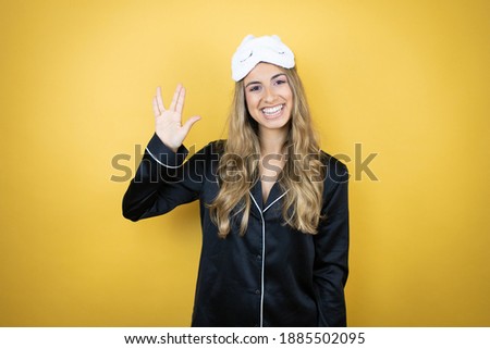 Young pretty woman wearing sleep mask and pajamas over isolated yellow background doing hand symbol