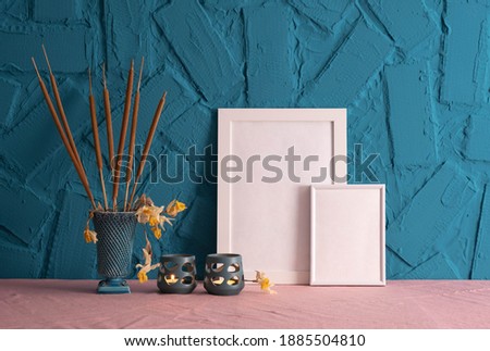 candlesticks, decoration of reed cones and white frames for a photo standing on a table, on a blue background