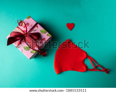 Pink box with a gift tied with a red ribbon next to a red heart and a red mask on an orange background