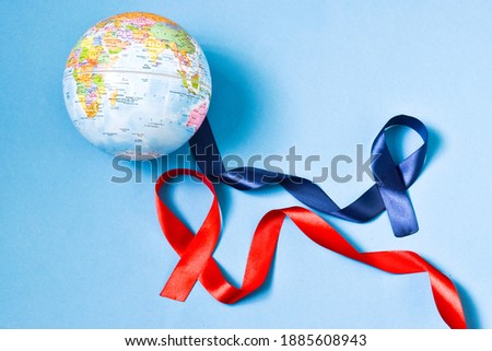 World Cancer Day. Cancer awareness. Blue with red ribbons and globe on a blue background. International Agency for Research on Cancer.World cancer day and medicine concept. Copy space, flat lay.