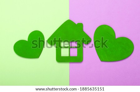 Green wooden hearts with a house figurine on pink green pastel background