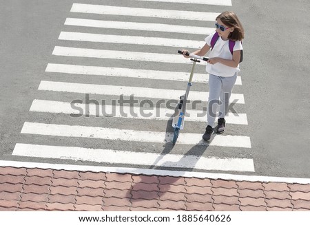 Girl carrying scooter and crossing road on way to school. Zebra traffic walk way in the city. Pedestrian passing a crosswalk. Healthy lifestyle. Eco-friendly transport. Safety concept for road  users