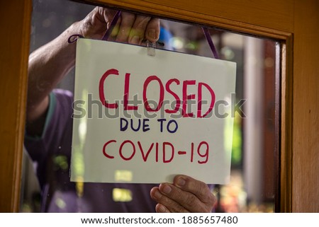 a man fixing temporary closed sign for covid-19 on shop window