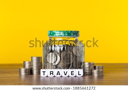 A lot coins in glass money jar with yellow background. Saving for Travel concept.
