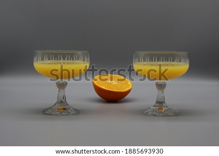 two elegant vintage glasses with illuminating yellow orange juice. half of orange in the middle. ultimate gray background