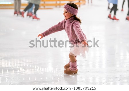 little girl in a pink sweater is skating on a winter evening on an outdoor ice rink lit by garlands