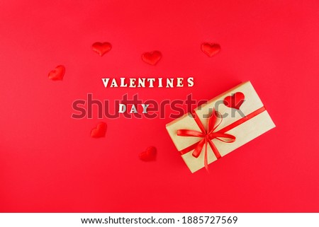 Gift on a red background. The inscription "Valentine's Day". Wooden letters.