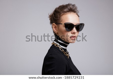 High fashion photo of a beautiful elegant young woman in a pretty yellow leather long skirt, black blouse, stylish sunglasses, accessories, boots posing over white, soft gray background. Studio Shot. 