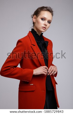 High fashion photo of a beautiful elegant young woman in a pretty suit, red jacket, black transparent blouse with a bow, short pants posing over white, soft gray background. Studio Shot.