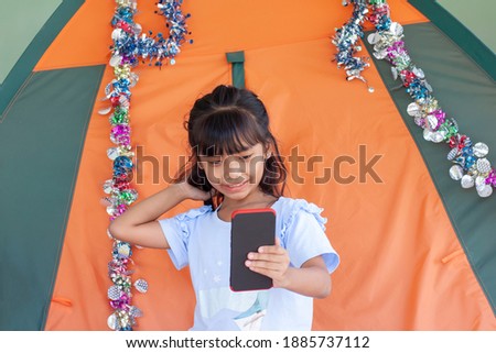 Asian little girl used mobile phone taking a selfie in front of the tent while going to travel on holiday.